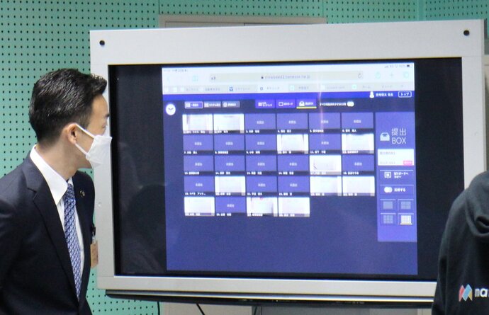 事業視察の際に杉島市長が大型ディスプレイの画面を眺めている様子を撮影した写真、画面には四角いアイコンが多数映ったアプリケーションが映し出されている