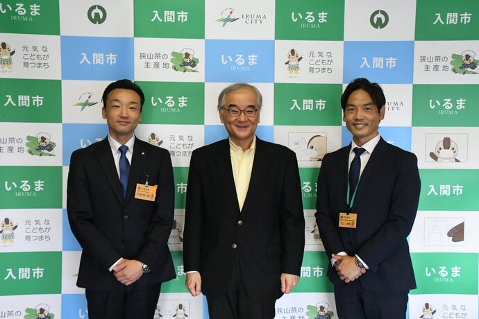 DX研修の際に入間市と書かれたパネルの前で左から杉島市長、京都芸術大学本間教授、市の関係者の計3名の男性が横一列に並んでいる姿を撮影した写真