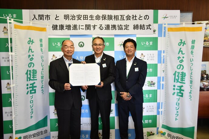 笑顔の男性3人のうち2人が連携協定の書類を掲げている写真