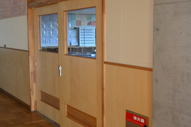 黄土色の木製の引き戸があり、引き戸の窓から教室の室内が見えている様子を、廊下側から撮影した写真