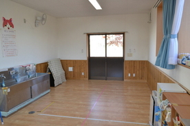 奥に引き戸、左に手洗い場とその上に壁掛け扇風機、右に低い棚が設置された、フローリングの床で構成された部屋の様子を、撮影した写真