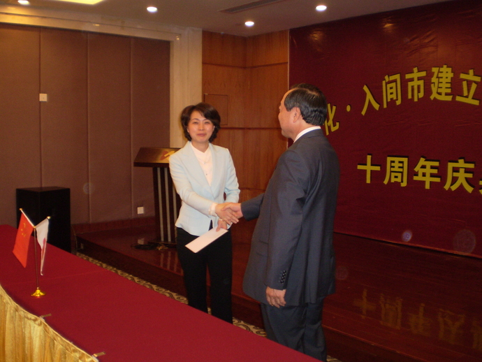 机の上に日本の国旗と中華人民共和国の国旗があり、男性と女性が笑顔で握手をしている写真。