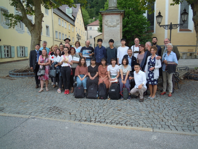 ミュンヘンのマリエン広場にあるベンチを囲んで、日本人学生8名、引率の男性2名、受け入れ先のヴォルフラーツハウゼン市民が20名、集まっている。日本人の女子学生5名はベンチに腰掛け、男子学生3名と引率の男性2名はベンチの後ろや横に位置取っている。ヴォルフラーツハウゼン市民は日本人学生を挟む形で、向かって左に13人、右に7人に別れて並び、街並みをバックにして撮影された記念写真。