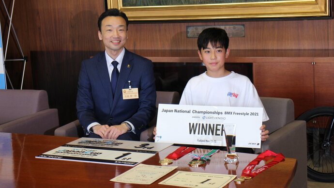 市長の男性と、WINNERと書かれた紙を持っている男の子が並んで着席している写真