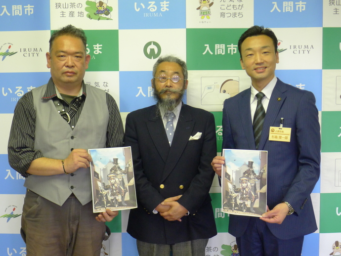 イラストが描かれた紙を持って、三人の男性が並んで立っている写真