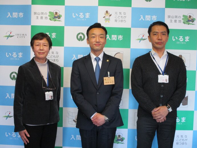入間市と書かれたパネルの前で左から齋藤委員、杉島市長、西澤委員の計3名が横一列に並んでいるのを撮影した写真
