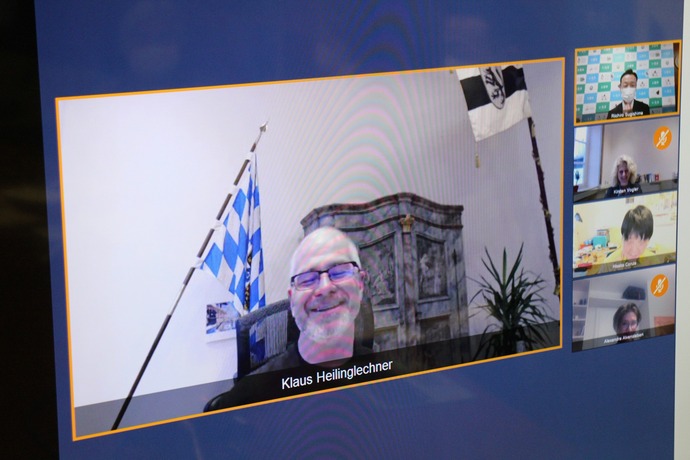 白髪の眼鏡をかけた外国人男性が大きく写っている、ウェブ会議の画面を撮影した写真