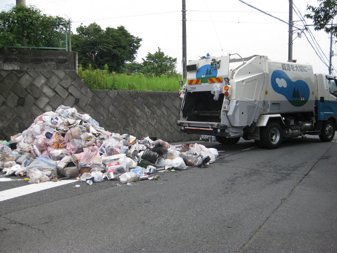 ゴミ収集車と、道路に山積みになったゴミが写った写真。