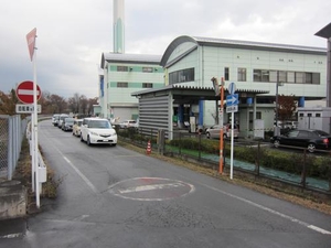 薄い水色の建物の敷地の外に車がたくさん並んで混雑している様子の写真