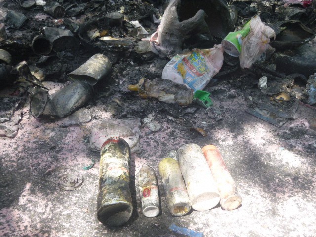 スプレーによるパッカー車火災の写真。焦げたスプレー缶5本が道路に並べられている。
