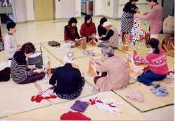 室内に畳の敷物を敷いてたくさんの人がその上に輪になるように座り布ぞうりを作っている様子の写真