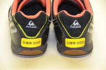 かかとステッカーの写真。靴の踵部分に「入間市000」と印字された黄色いシールが貼られている。