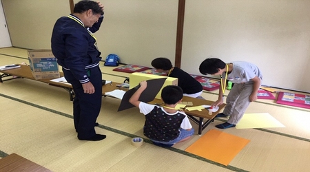 第3回子どもスタッフ会議の様子の写真。子ども三人と大人一人が、和室に置かれた長机に画用紙などの工作道具を広げ、準備をしている。