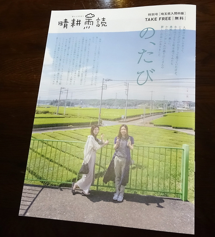 田んぼのそばにある柵に寄りかかっている2人の女性が表紙になっている冊子が机に置かれている写真