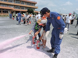 消火器を持った子供に消化を指導する様子の消防団員の写真