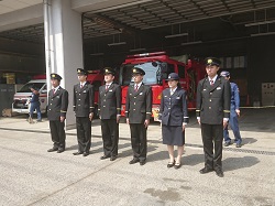 消防車の前で整列する制服姿の男女の消防団員の写真