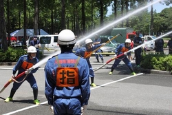 消防団員が持ったホースの先から勢いよく水が放水されている写真