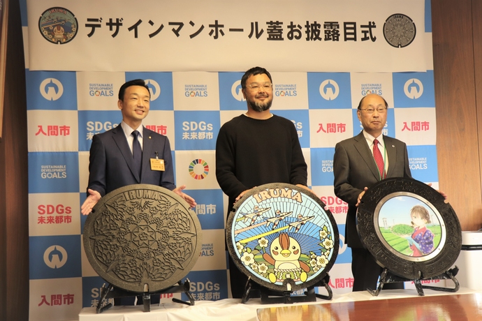 左から杉島市長、いるティーデザインとひばりデザインを担当した新田氏、濱川副市長が並んでマンホールのふたを見せている、デザインマンホール蓋のお披露目式の写真