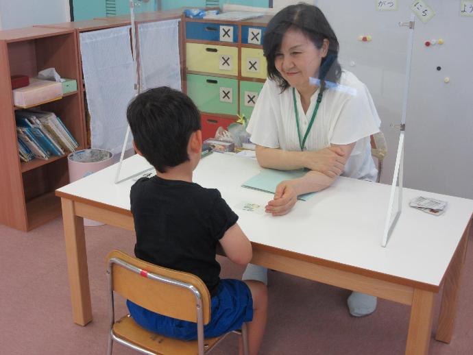 女性と男の子がアクリル板越しにイラストカードで学んでいる写真