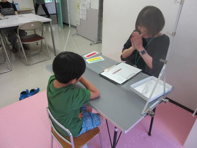 女性が男の子と一緒にアクリル板越しで口の運動をしている写真