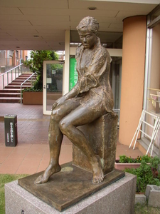 公民館の入り口付近に展示されている、顔がうつむいたまま座っている女性のブロンズ像の写真