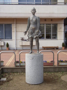 石の円柱の上に立つ少女を象ったブロンズ像が建物の前に展示されている写真