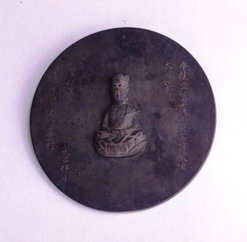 文字と仏様が掘られた黒い円盤の写真