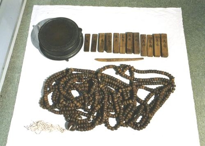 長い数珠と複数の文字が書かれた木の板と鰐口が並べられた写真