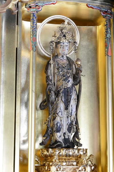 金色のケースに入った朽ちかけた木造の観音菩薩立像の写真