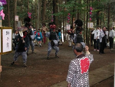 「獅子舞」と書かれた看板と林の中で法被を着た人たちが踊っている写真