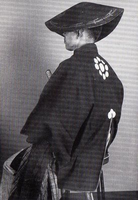 笠を被った和装の男性の斜め後ろ姿のモノクロ写真