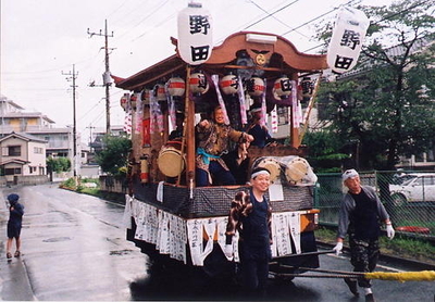 「野田」と書かれた提灯の付いた山車に乗った人たちと、山車を引く人たちの写真