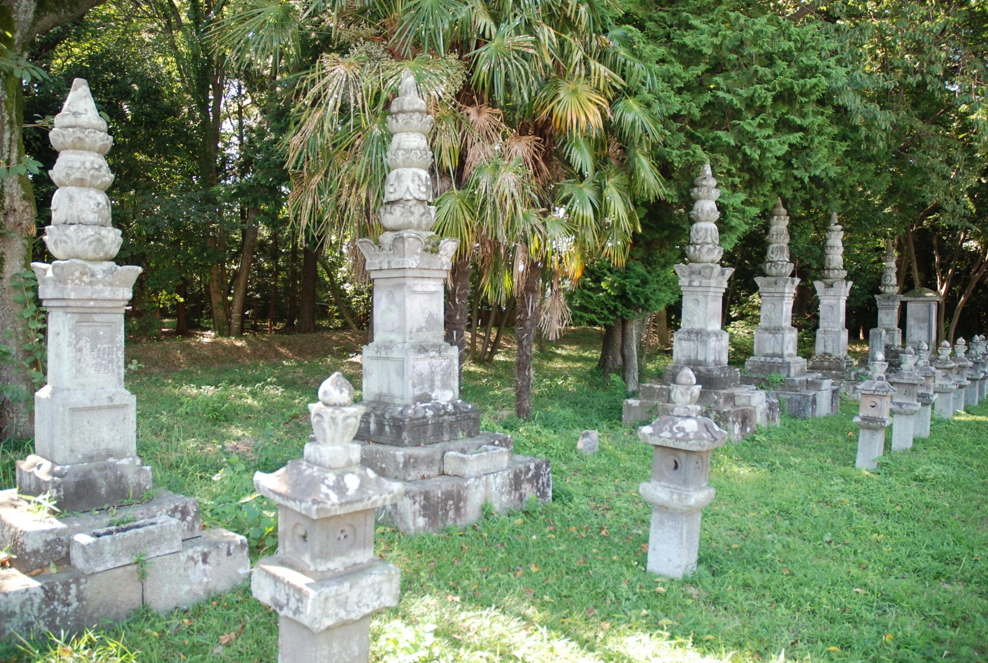 木々に囲まれた草地の上に立つ複数の印塔の写真