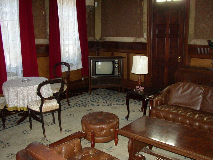 ダイヤル式テレビや赤いカーテン、卓上ランプ、クロスの付きテーブル、茶色で統一された家具の置かれた西洋館の室内の写真