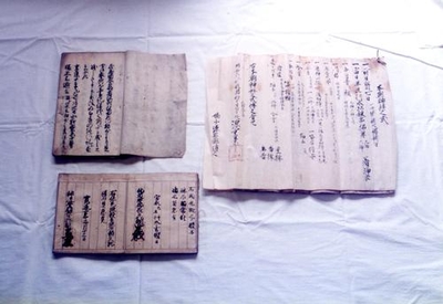 三種の古い文書の見開きが白いテーブルクロスの上に並べられている写真