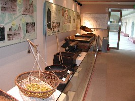 籠や木でつくられた道具と解説パネルが、博物館の壁沿いに展示されている写真