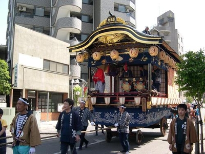 昼の町の中、山車を引く男性たちの写真